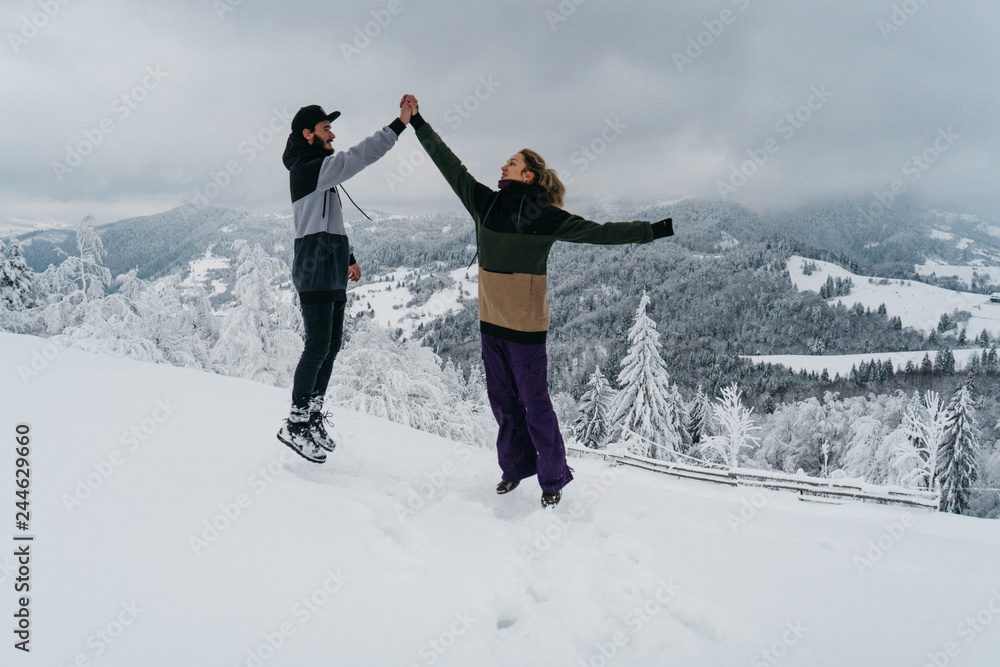 Couple of man and woman giving high five on the top of the mountain with the scenic view. Beautiful snowy mountains in winter
