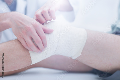 Mid section of doctor bandaging leg of patient in hospital