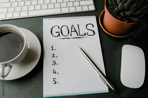 Картината върху платно Top view of notepad with Goals List, cup of coffee on dark gray table, goals con