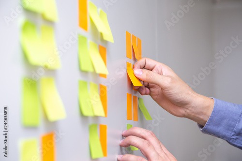 IT worker tracking his tasks on kanban board. Using task control of agile development methodology. Man attaching sticky note to scrum task board in the office