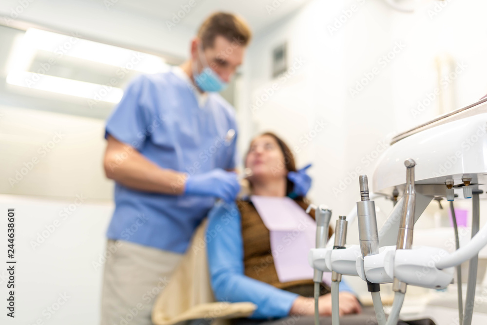 Dentist performing teeth treatment with female patient blurred, focus on tools Dentist performing teeth treatment with female patient blurred, focus on tools