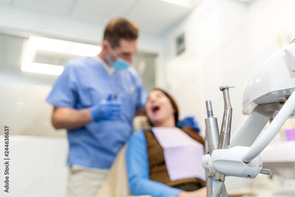 Obraz premium Dentist performing teeth treatment with female patient blurred, focus on tools