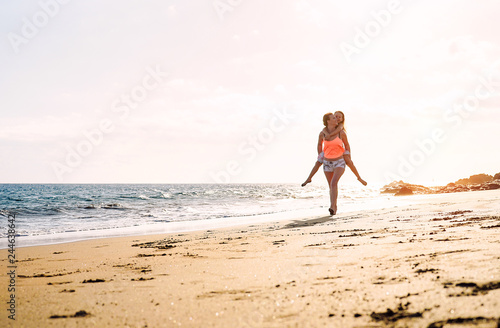 Happy loving family mother and daughter running and having fun on the beach at sunset - Mom piggyback her kid next to ocean during holidays - Parent, vacation, family lifestyle concept