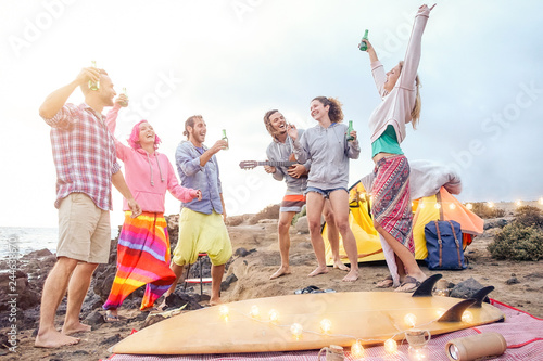 Happy friends having fun playing guitar and dancing on the beach - Group of young people making party drinking beers while camping with tent - Travel, vacation and youth holidays lifestyle concept photo