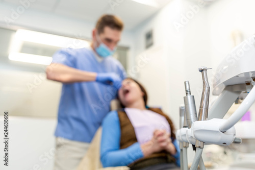 Dentist performing teeth treatment with scared female patient blurred  focus on tools