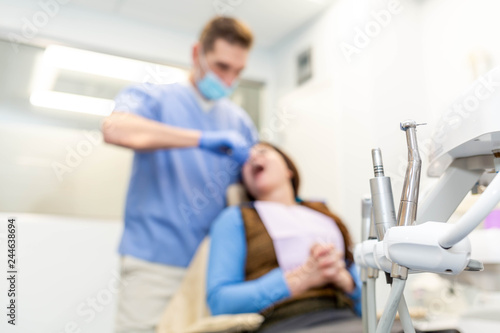 Dentist performing teeth treatment with scared female patient blurred  focus on tools