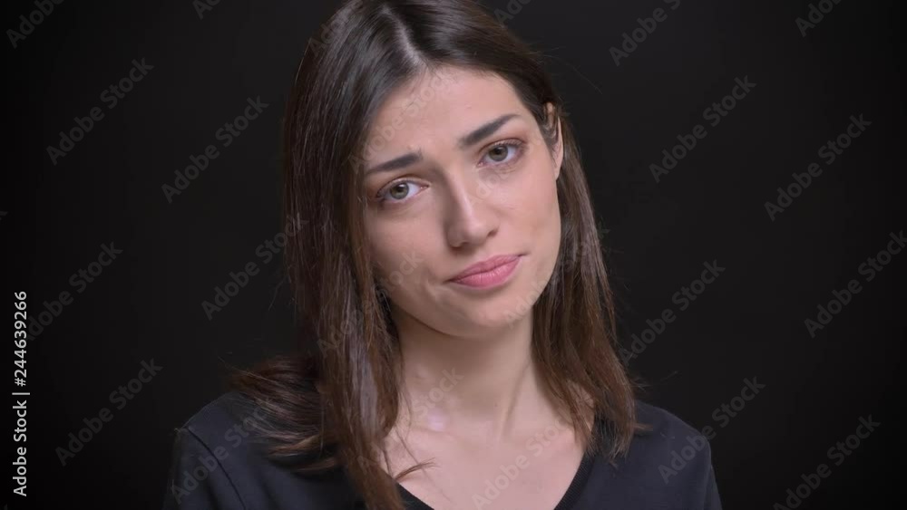 Close-up portrait of young caucasian long-haired brunette girl watching shyly into camera on black background. Close-up portrait of young caucasian long-haired brunette girl watching shyly into camera on black background.