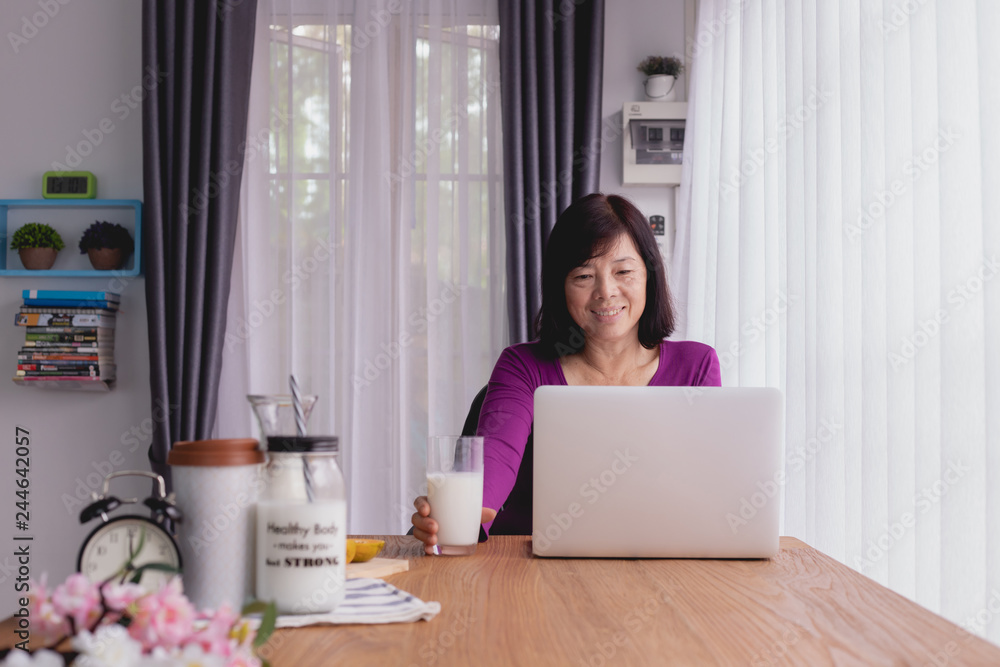 Asian Elderly using laptop and drinking milk at home. Asian Elderly using laptop and drinking milk at home.