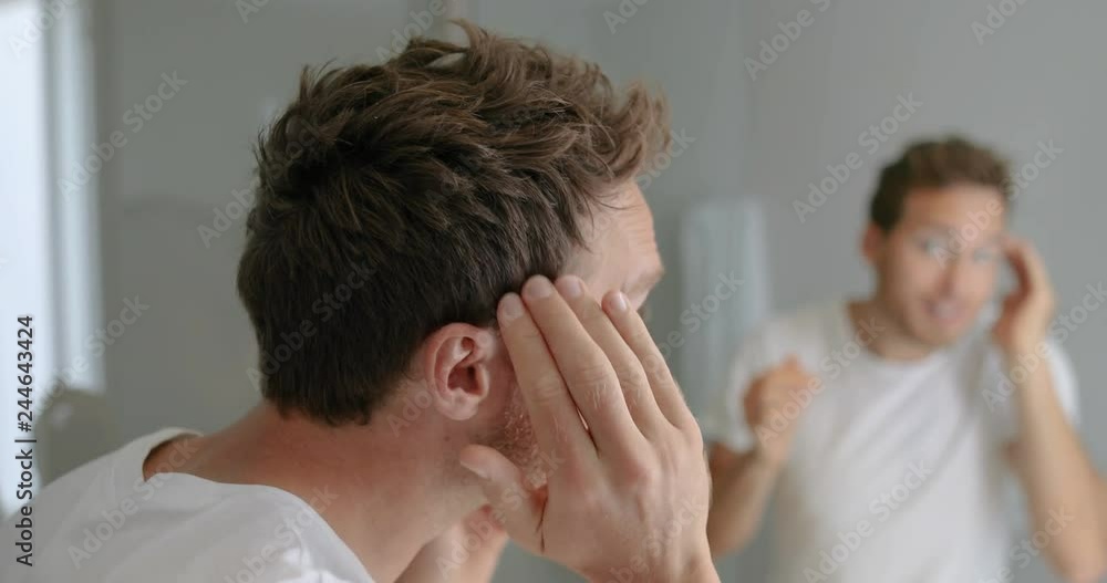 Man looking in bathroom mirror putting wax product touching his hair styling or checking for hair loss problem. Male problem of losing hairs. Man looking in bathroom mirror putting wax product touching his hair styling or checking for hair loss problem. Male problem of losing hairs.