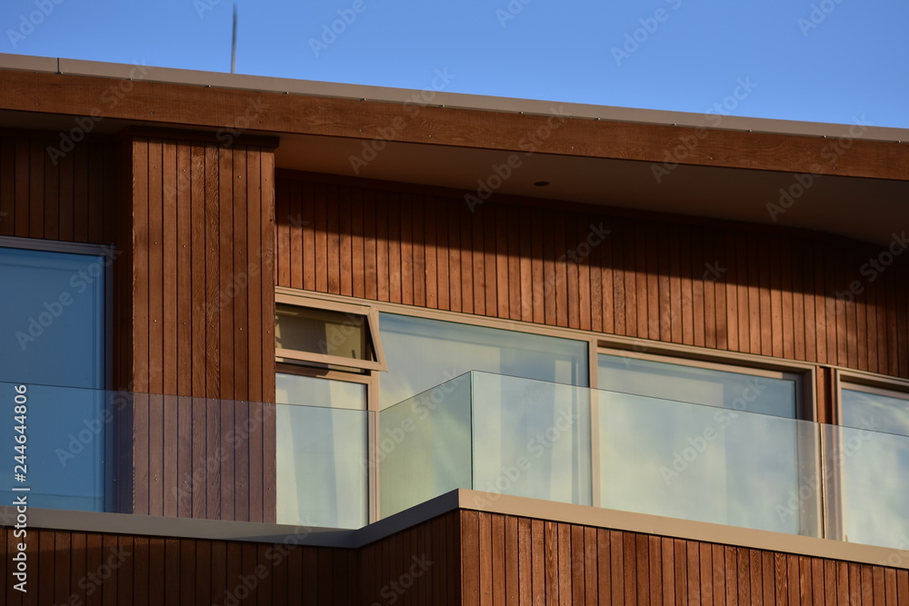 Facade with windows and veranda of modern wooden house with vertical varnished cladding and glass transparent railing. - obrazy, fototapety, plakaty 