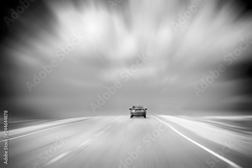 Rear View of a Car Speeding on Asphalt Road in Countryside. Cloudy, Stormy Sky. Black-and-White Image with Copy-Space. Motion Blur.