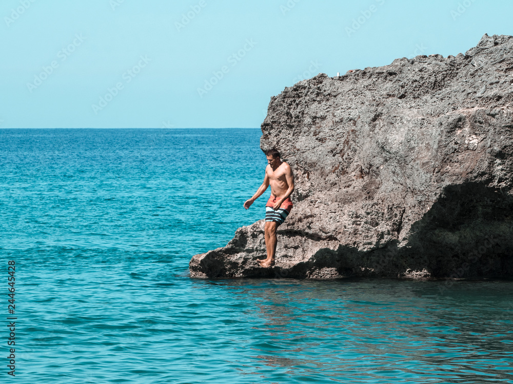A man jumps from a cliff into the ocean.
