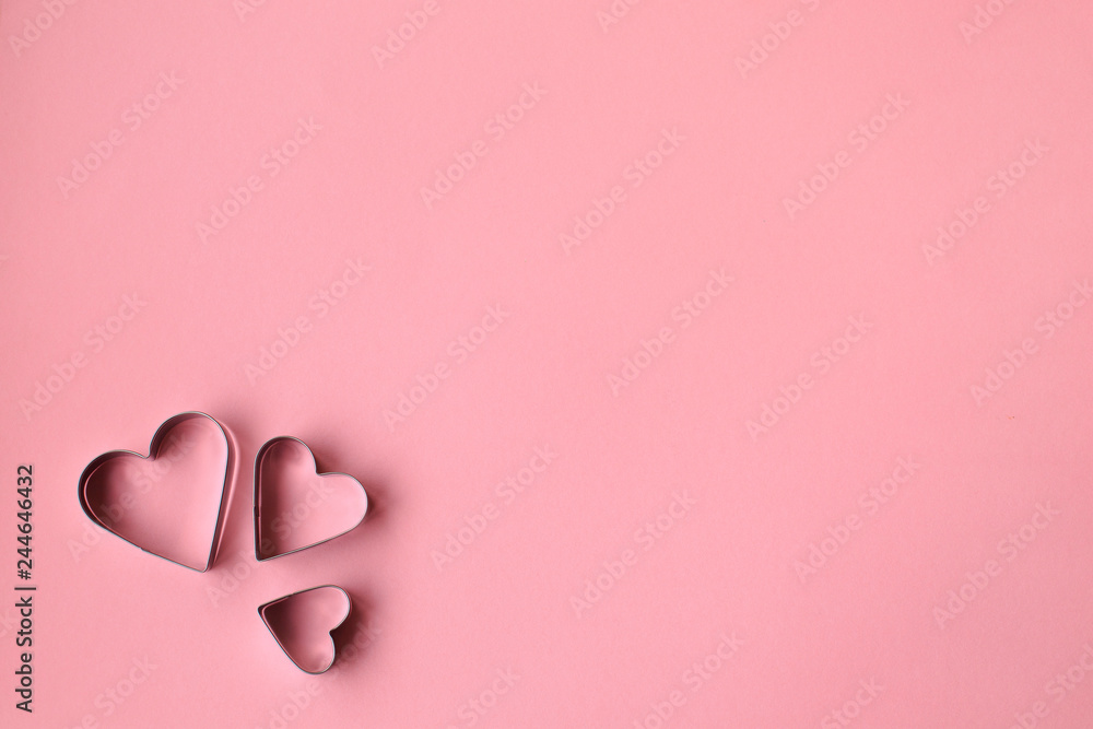 Three heart shaped cookie cutters over a pink background. Valentine's Day.