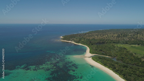 Aerial view of beautiful tropical beach Saud with turquoise water in blue lagoon, Pagudpud, Philippines. Ocean coastline with sandy beach and palm trees. Tropical landscape in Asia.