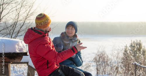 A man and a woman throw up snow and have fun outdoors with a view of the river. Frosty sunny winter day