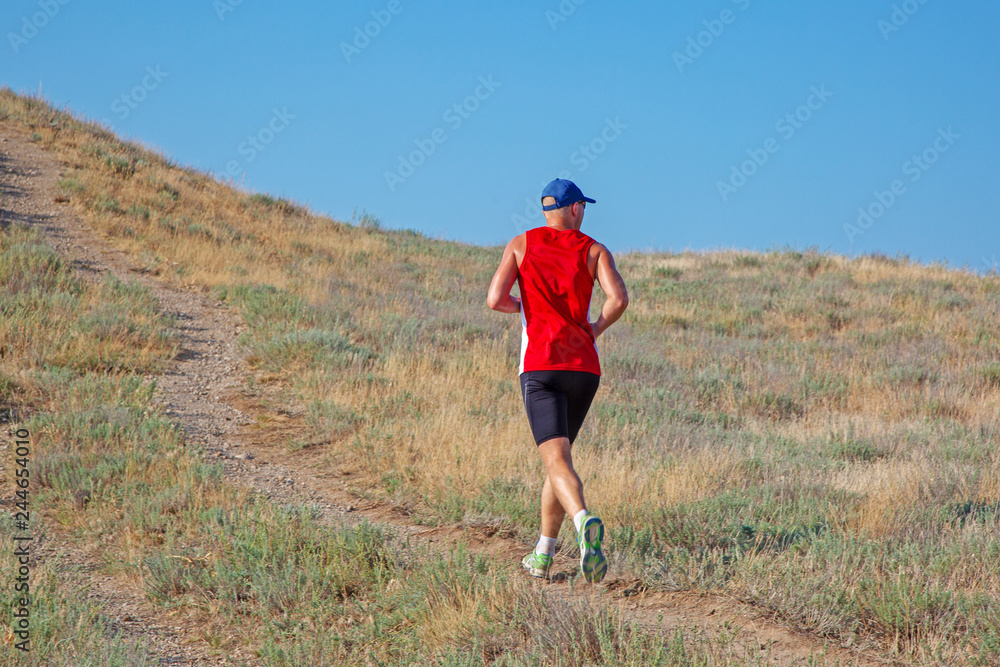 rear view of athletic runner running on a mountain trail on a blue sky background rear view of athletic runner running on a mountain trail on a blue sky background