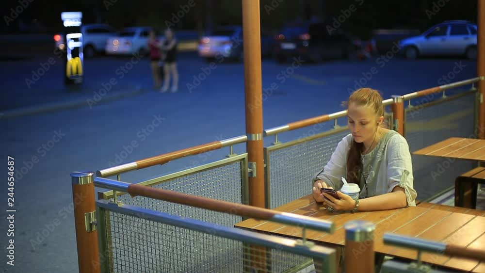 young single woman sitting in the evening in a summer cafe on the street , listening to music on smartphone and have dessert. young single woman sitting in the evening in a summer cafe on the street , listening to music on smartphone and have dessert.