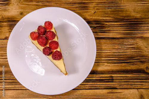 White plate with cheesecake New York and raspberries on wooden table. Top view