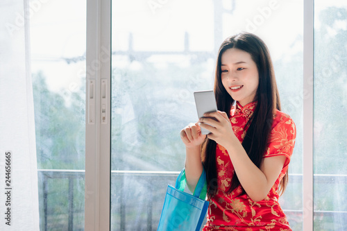 Smile of Portrait Beauty Asian Woman with Chinese dress,Qipao,Cheongsam Chinese New Year Using Smartphone Technology Shopping Online and hold Bag Sitting near Window in Clean White Room,Copy Space. Free Download Smile of Portrait Beauty Asian Woman with Chinese dress,Qipao,Cheongsam Chinese New Year Using Smartphone Technology Shopping Online and hold Bag Sitting near Window in Clean White Room,Copy Space. - GFXLoad