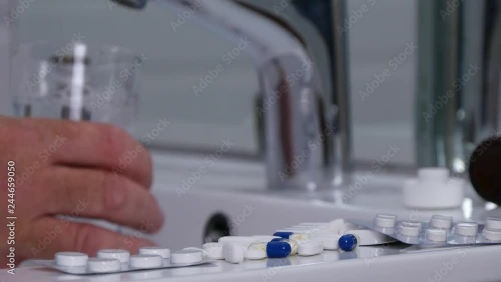 Man Making a Medical Cure Put Water in a Glass from the Sink in a Bathroom Man Making a Medical Cure Put Water in a Glass from the Sink in a Bathroom