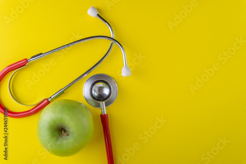 Green Apple with medical stethoscope isolated on yellow background for healthy eating. Selective focus and crop fragment. Healthy, Diet and copy space concept photo