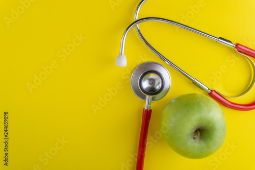 Green Apple with medical stethoscope isolated on yellow background for healthy eating. Selective focus and crop fragment. Healthy, Diet and copy space concept photo