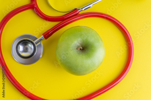 Green Apple with medical stethoscope isolated on yellow background for healthy eating. Selective focus and crop fragment. Healthy, Diet and copy space concept photo