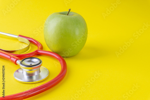 Green Apple with medical stethoscope isolated on yellow background for healthy eating. Selective focus and crop fragment. Healthy, Diet and copy space concept photo