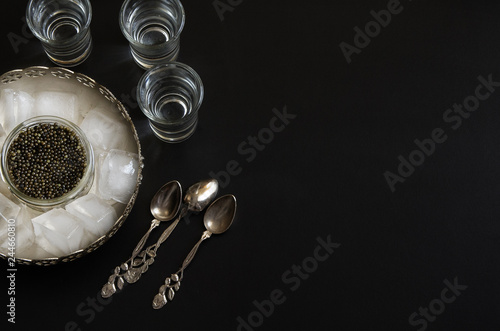 Russian beluga caviar served in silver bowl with ice and vodka. Black caviar delicatessen background.