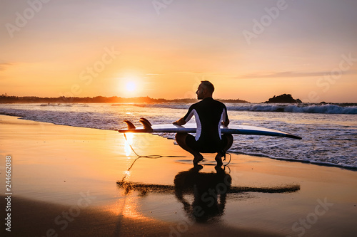 Surfer with surfboard sits on ocean surf line at sunset time © Soloviova Liudmyla