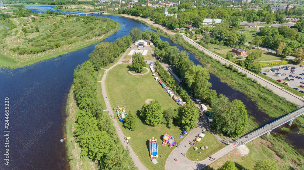 Aerial drone view of summer festival being set up next to river or lake. Sunny day by the water, blue sky. Concept of summer holidays, travelling and vacation. 