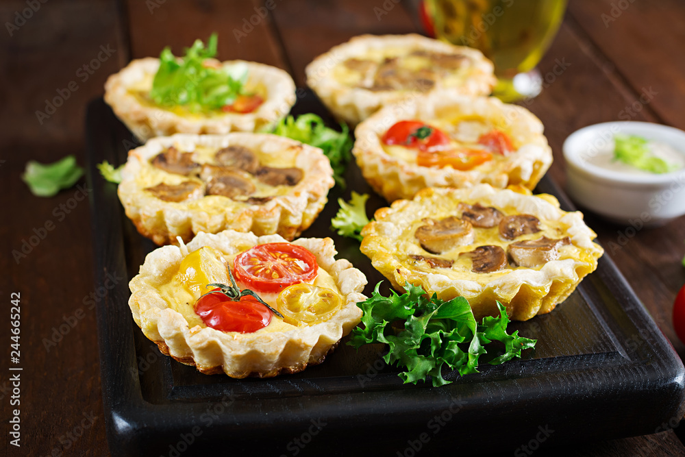 Mushrooms, cheddar, tomatoes tartlets on wooden background. Mini pies. Delicious appetizer, tapas, snack. Mushrooms, cheddar, tomatoes tartlets on wooden background. Mini pies. Delicious appetizer, tapas, snack.