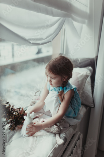 Pretty girl sitting near window and playing with soft toy, intdoor photo