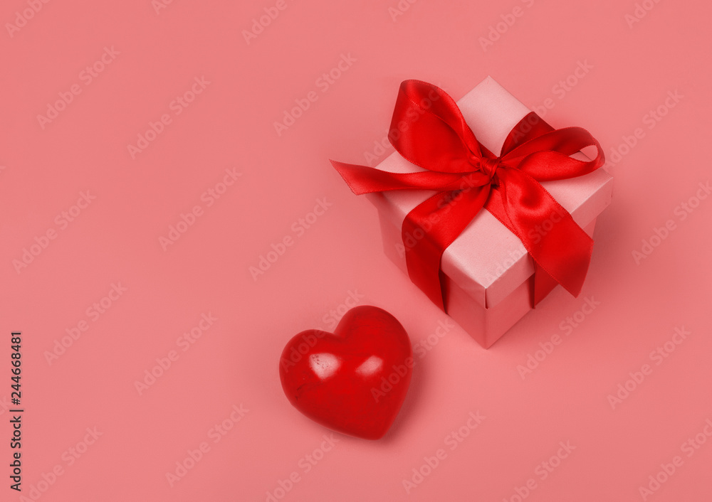 Gift or present box with red bow ribbon and glitter heart on living coral background for Valentines day