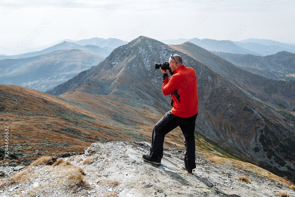 Obraz premium A young man sports athlete stands on the mountain and photographs beautiful landscapes