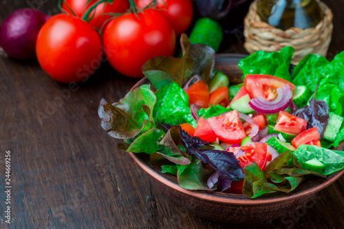 Salad with fresh vegetables, garden herbs and sun-dried tomatoes in a clay bowl on a dark wooden background