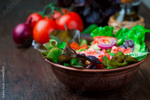 Salad with fresh vegetables, garden herbs and sun-dried tomatoes in a clay bowl on a dark wooden background