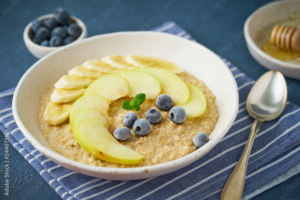 Oatmeal with bananas, blueberries, jam, honey, blue napkin on blue stone background. Close-up, side view Oatmeal with bananas, blueberries, jam, honey, blue napkin on blue stone background. Close-up, side view