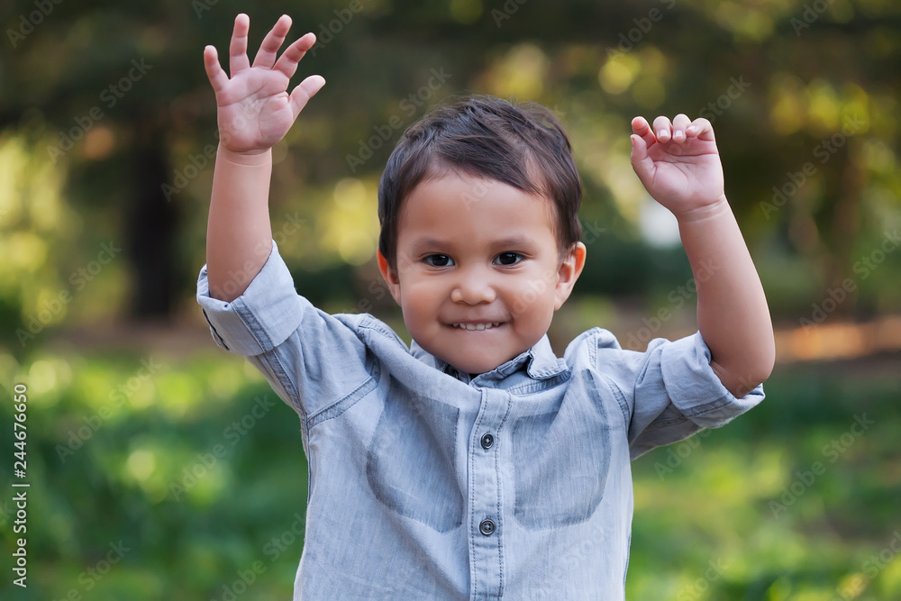 A handsome young boy, nicely dressed showing an expression of joy with hands up in the air looking excited and happy to be playing outdoors. A handsome young boy, nicely dressed showing an expression of joy with hands up in the air looking excited and happy to be playing outdoors.