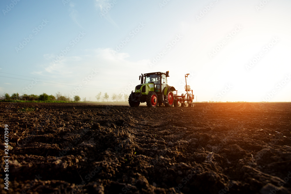 Fototapeta premium Farmer sowing crops at field with tractor. - Image