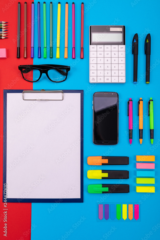Flat lay composition of business desk with smartphone, clipboard, stickers, and pen on colorful blue and red background Flat lay composition of business desk with smartphone, clipboard, stickers, and pen on colorful blue and red background