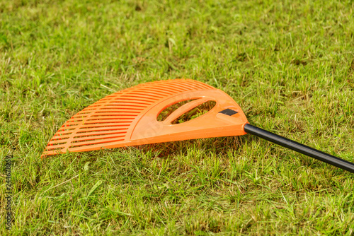 Orange rake on stick collecting grass, garden tools