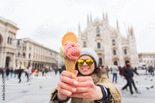 Young and happy female tourist standing with ice-cream in front of the famous Duomo cathedral in Milan. Happy vacations in Milan