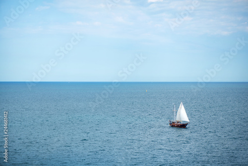 Viking style yacht with sails leaving the coast for open sea. Nostalgic mood. Horizon and blue sky background on summer day