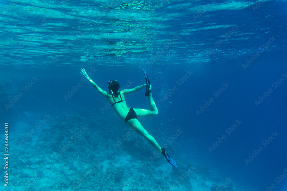 Underwater. Young woman snorkeling gliding over vivid coral reef on a breath hold