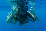 Young woman snorkeling making okay signs underwater near coral reef in blue sea. Underwater