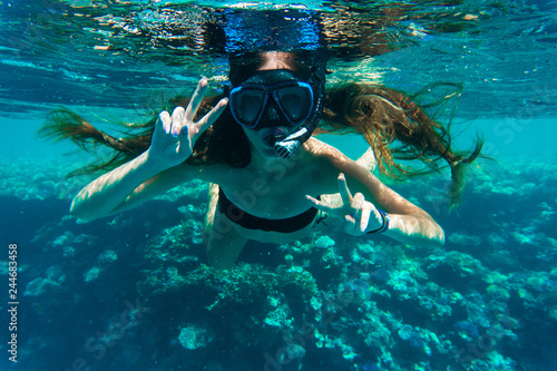 Young woman snorkeling making peace signs underwater near coral reef