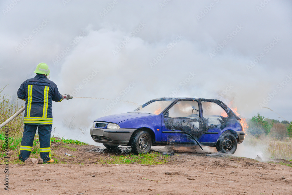 Fire fighter prepare to attack a propane fire. Burning and crashed car after explosion. Accident on street at countryside. No one was injured. Artificially created set for film making