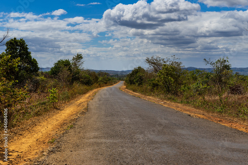 Typical road in Middle Vietnam. On the road are holes. Along the road are forest and red clay. Cloudy weather and sunshine. The picture was taken on January 2019 near village Pleiku.