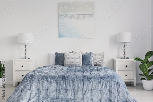 Symmetry in design of elegant new york style bedroom with king size bed with velvet bedding, white bedside tables and abstract painting on the wall photo